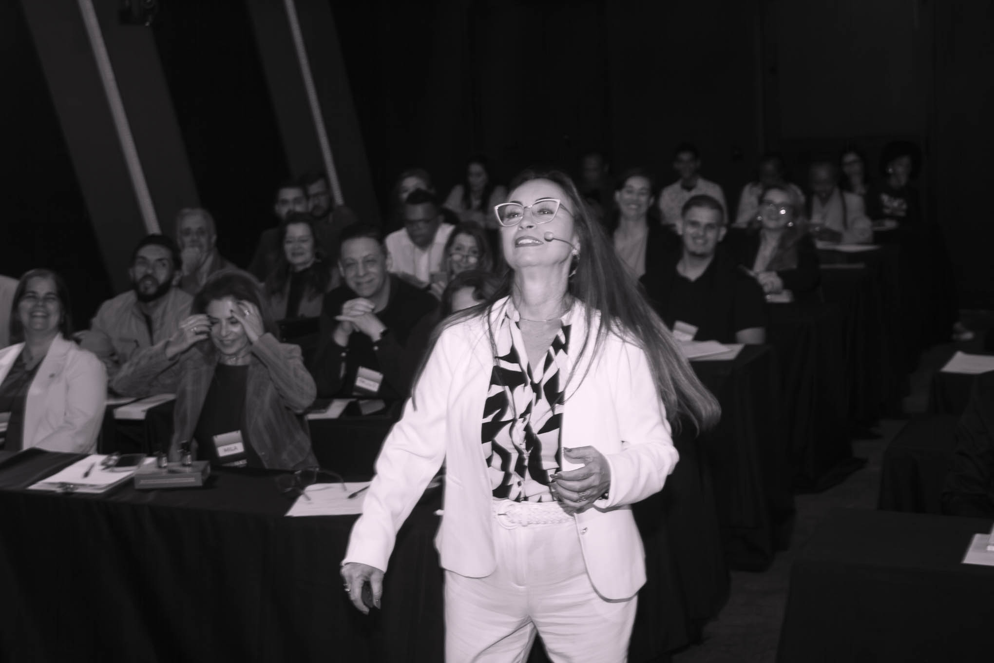 Eunice Reis andando pelo palco com microfone de lapela durante a Imersão Fullness, em preto e branco